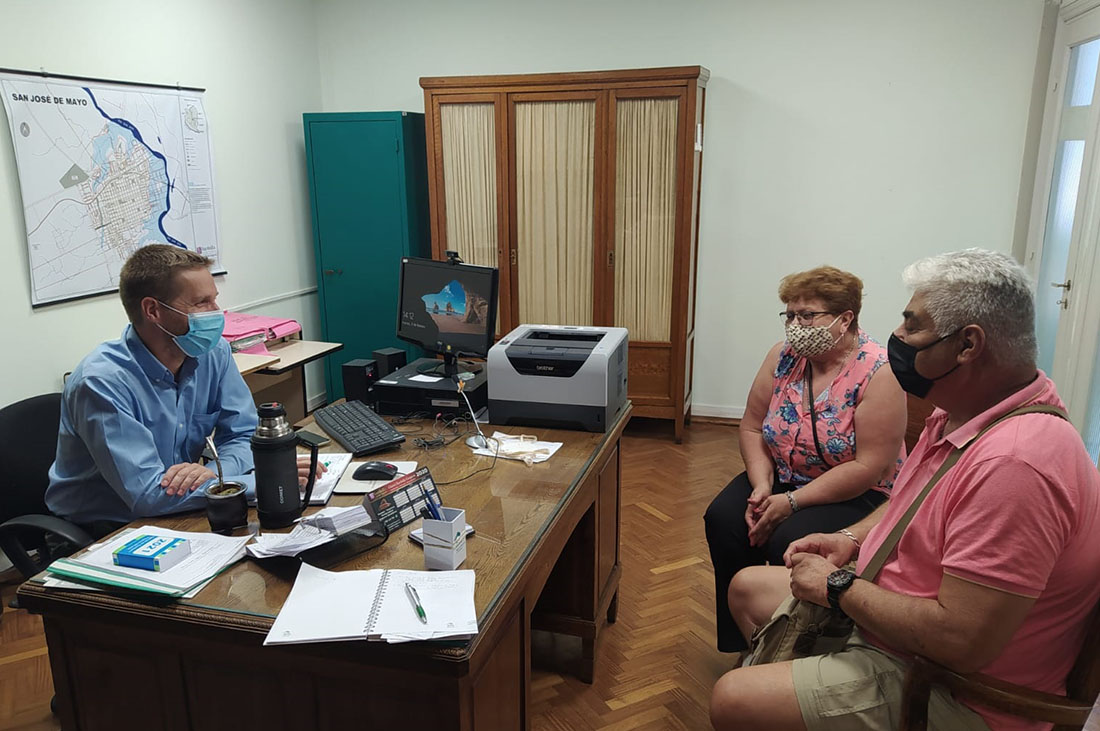 Presidente Mill sentado detrás de un escritorio, conversando con un vecino y una vecina.
