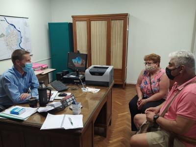 Presidente Mill sentado detrás de un escritorio, conversando con un vecino y una vecina.